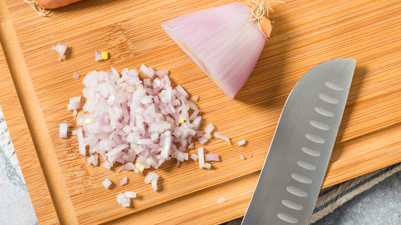 A half-diced shallot on a cutting board next to a knife.