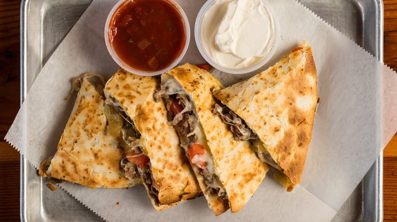 A steak quesadilla on a metal platter with sour cream and salsa