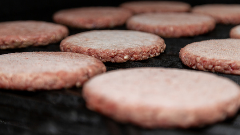 Several frozen burger patties cooking on a grill.