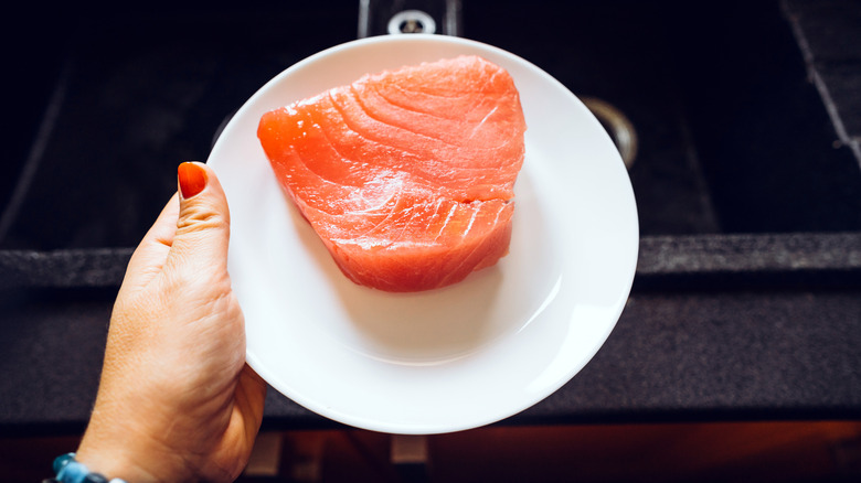 woman holds white plate of fresh salmon filet