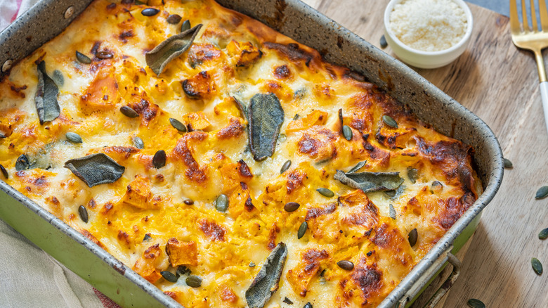 Lasagna decorated with sage leaves in a baking pan with parmesan cheese and a fork