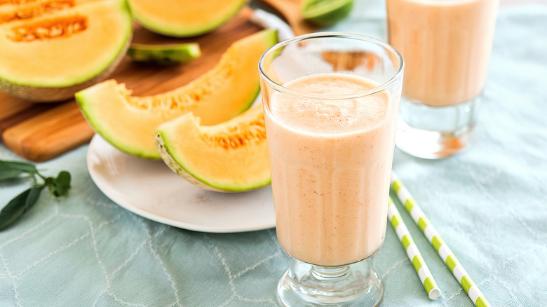 Glasses of cantaloupe smoothie on a blue tablecloth next to slices of cantaloupes