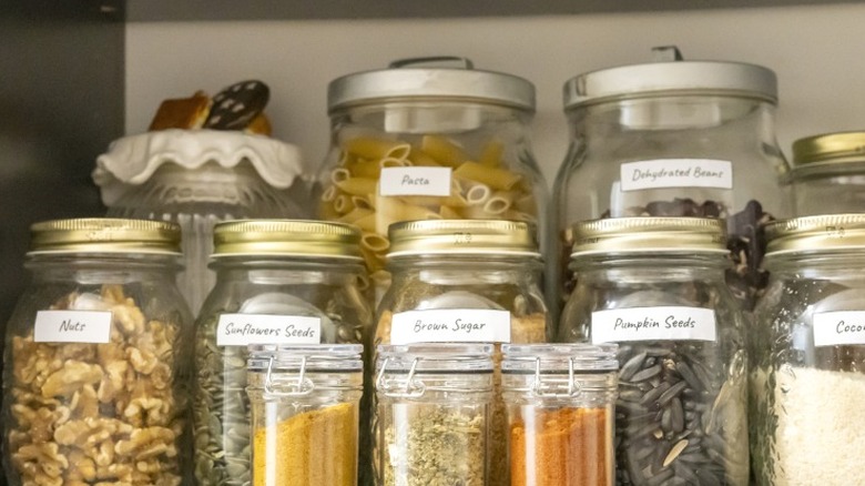 A number of foods and dry goods stored in jars in a pantry.