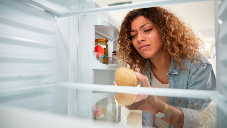 woman inspects yucky potato in fridge