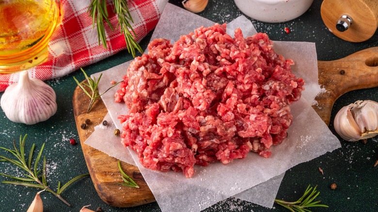 Raw ground beef on a cutting board with herbs and seasonings