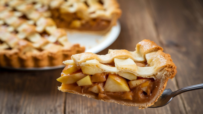 Slice of apple pie on a fork with a pie with the slice removed in the background