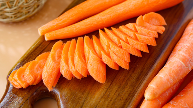Fresh, vibrant orange carrots, both whole and neatly sliced with decorative cuts, arranged on a wooden cutting board.