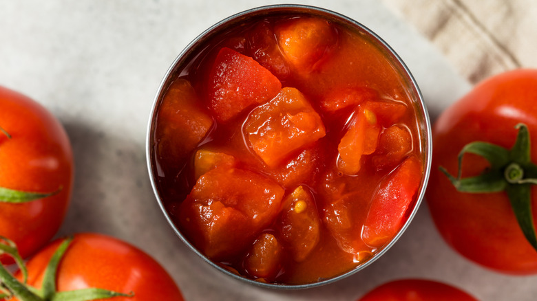 Overhead view of tomatoes in a can surrounded by whole tomatoes