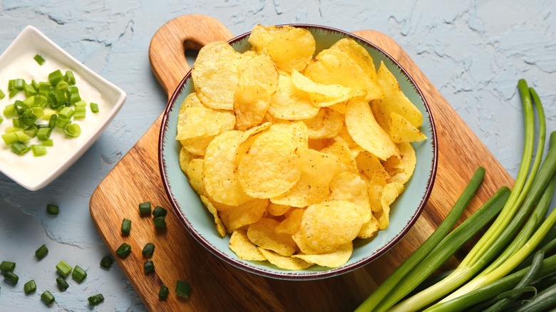 A bowl of plain potato chips next to some sour cream dip.