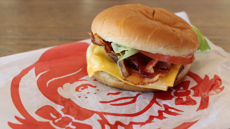 Hamburger with bacon, cheese, lettuce, and tomato on white with Wendy's red pigtailed girl logo