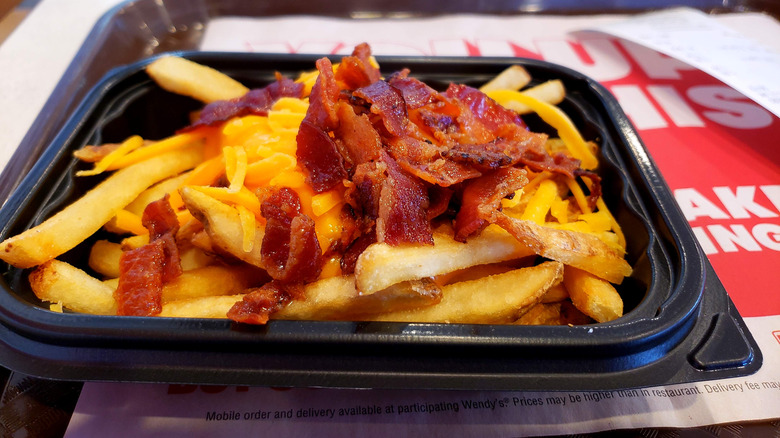 Wendy's fries with cheese and bacon in a square black plastic container on a tray with white and red paper