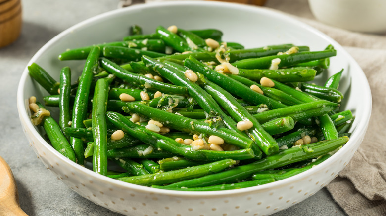 White bowl filled with cooked green beans topped with pine nuts