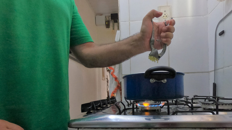 Person using garlic press right over pot on stove