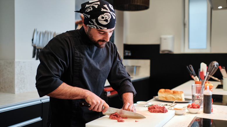 Side view of a chef in a black uniform preparing steak tartare