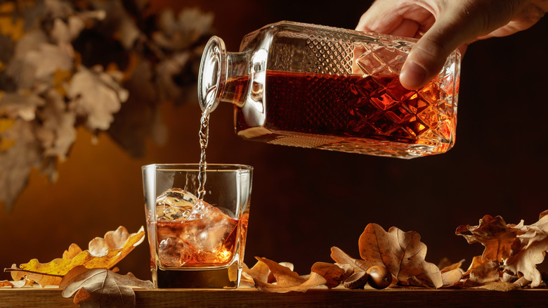 Whiskey being poured out of a decanter into a glass with ice in it