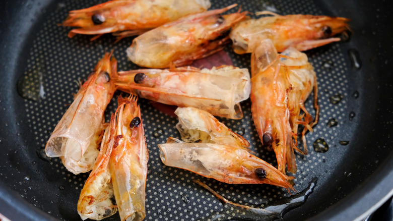 A closeup of cooked shrimp heads and tail shells in a frying pan