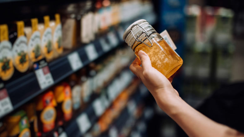 A person holding a jar of fresh honey at a grocery store.
