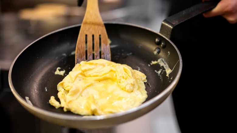 Person using a wooden spatula to cook fluffy scrambled eggs in a non-stick frying pan