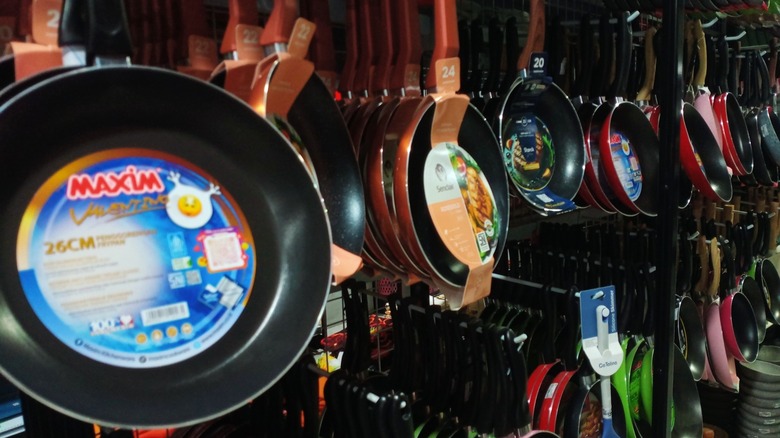 Various brands and sizes of non-stick frying pans hanging on display racks for sale inside a retail store