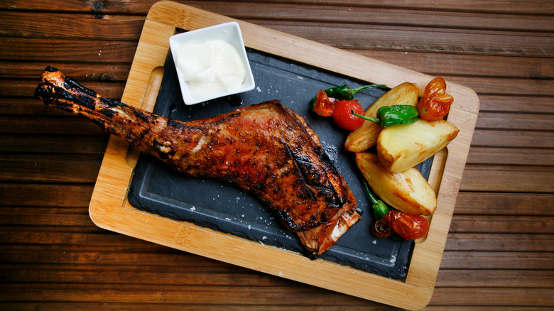 A bbq goat leg served with potatoes, veggies, and cream