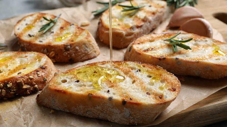 Olive oil being drizzled onto toasted bread with fresh rosemary