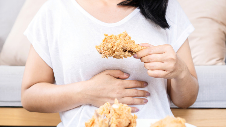 Person eating a piece of chicken and placing hand on stomach to signify fullness