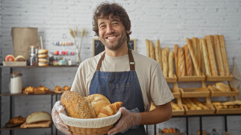A baker holds a basket of bread while smiling.