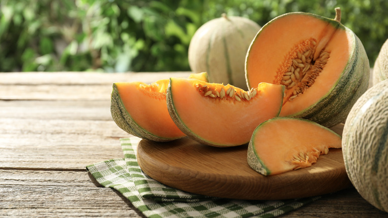 A cut up cantaloupe surrounded by other cantaloupes on a wooden table