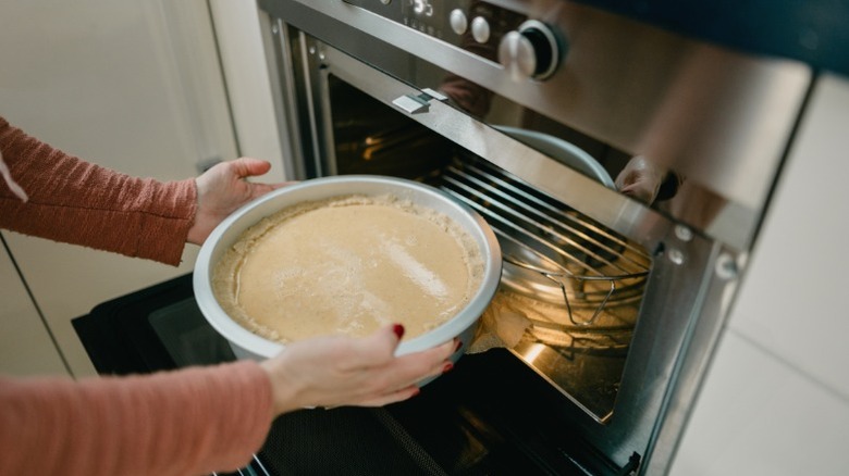 A woman puts a cheesecake in an oven
