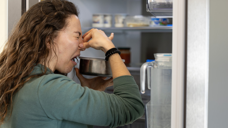 A woman holds her nose as she smells spoiled food