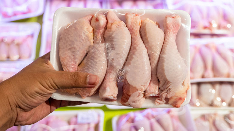 A shopper holds a package of raw chicken in front of a store meat display