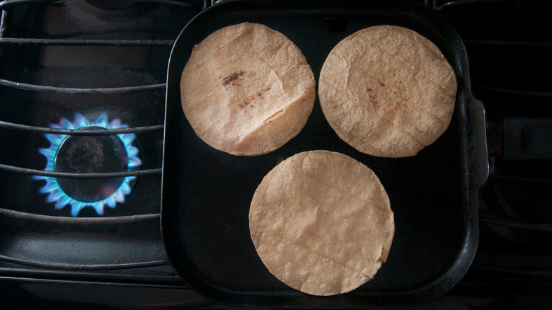 Corn tortillas warming on a comal on a gas stove