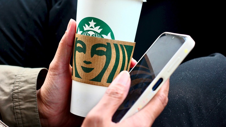 Person holding Starbucks cup while using cellphone