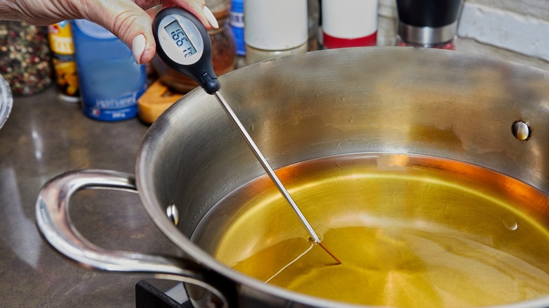 Hand checking the temperature of oil in a pot with a digital thermometer