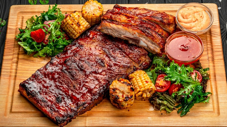 Ribs on wood board with sauces and roasted corn