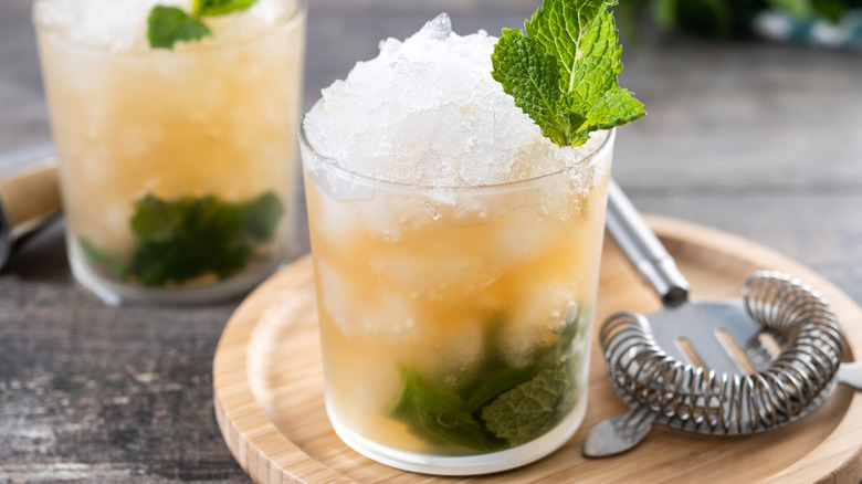 Two glasses of mint julep cocktail with a strainer sitting nearby.