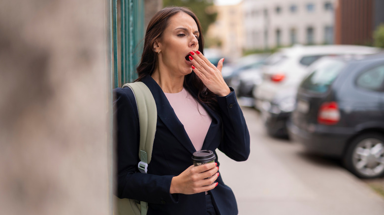 A yawning person holding a cup of coffee