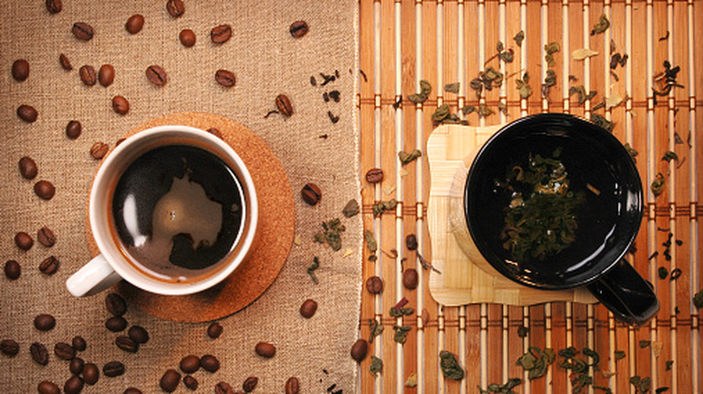 A cup of coffee surrounded by coffee beans pictured alongside a cup of tea surrounded by tea leaves