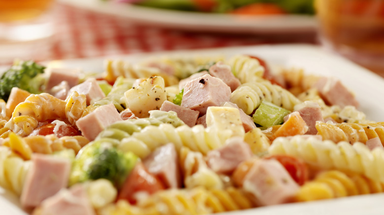 A bowl of deli-style pasta salad with assorted mix-ins on a picnic blanket