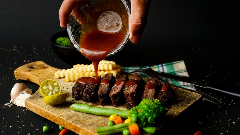 A chef pours sauce over pieces of steak with vegetables