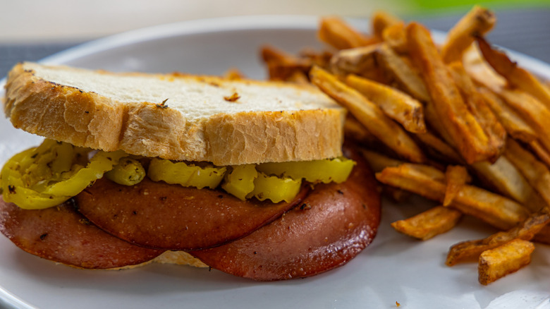 A fried baloney sandwich, with pickled peppers and a side of fries
