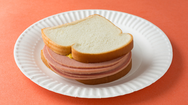 A baloney sandwich with mustard on a paper plate