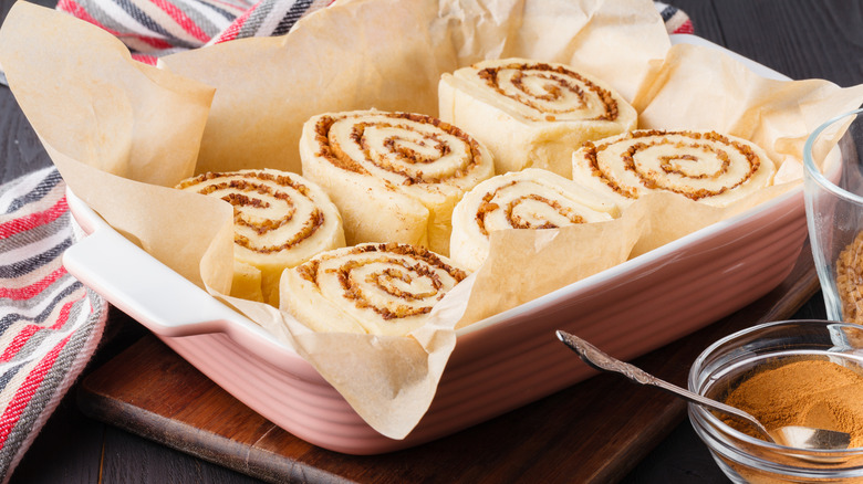 Six uncooked cinnamon rolls in a rectangular baking pan on a wooden board