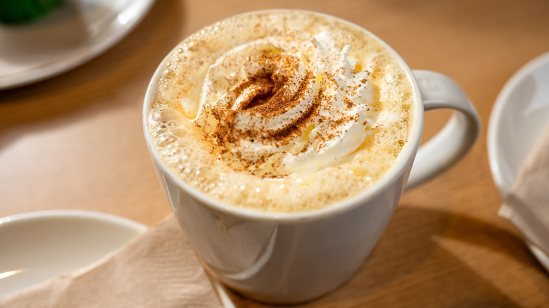White mug filled with foamy milk, topped with whipped cream sprinkled with spices