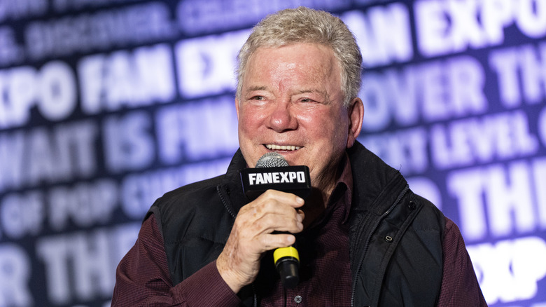 William Shatner holding a microphone and smiling at a Fan Expo event.