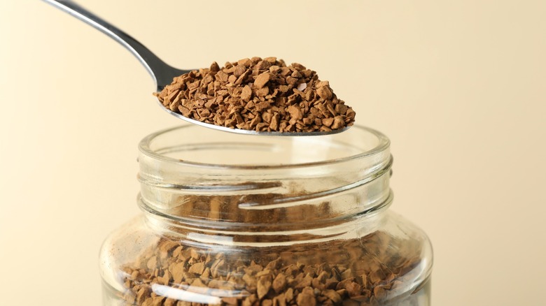Spoon scooping instant coffee from glass jar