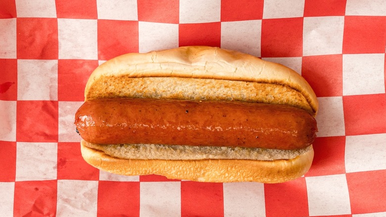 A hot dog in a bun viewed from above with a red and white checkered background.