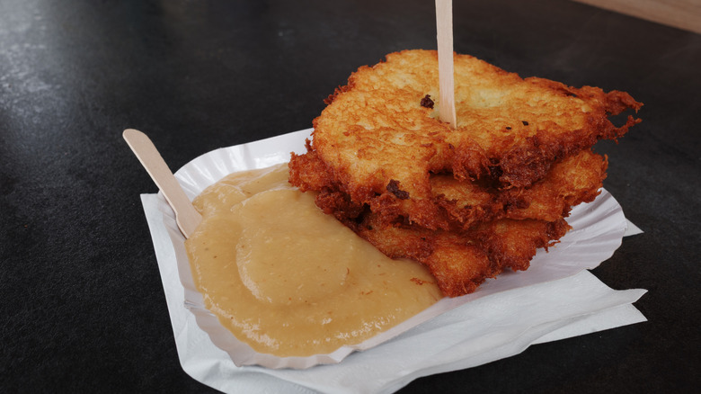 Apple sauce and three potato latkes on a white plate and white napkins on a black table