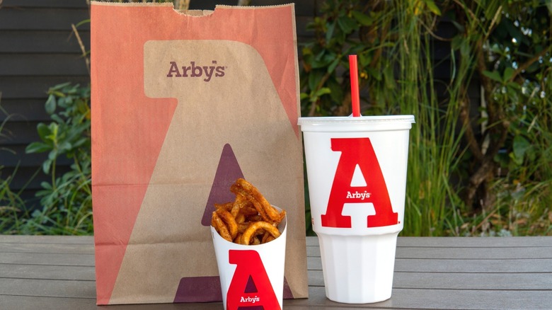 A bag of Arby's with curly fries and a drink.