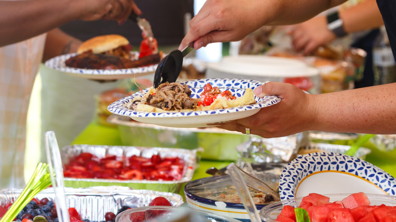 Hands put food on paper plate over potluck spread